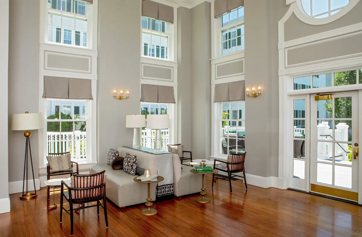 This image depicts a spacious, sunlit lounge with large windows, comfortable seating, and decorative lighting fixtures. A coffee table with elegant décor invites guests to gather, relax, and enjoy conversations. The overall mood is warm and sophisticated, ideal for communal activities.