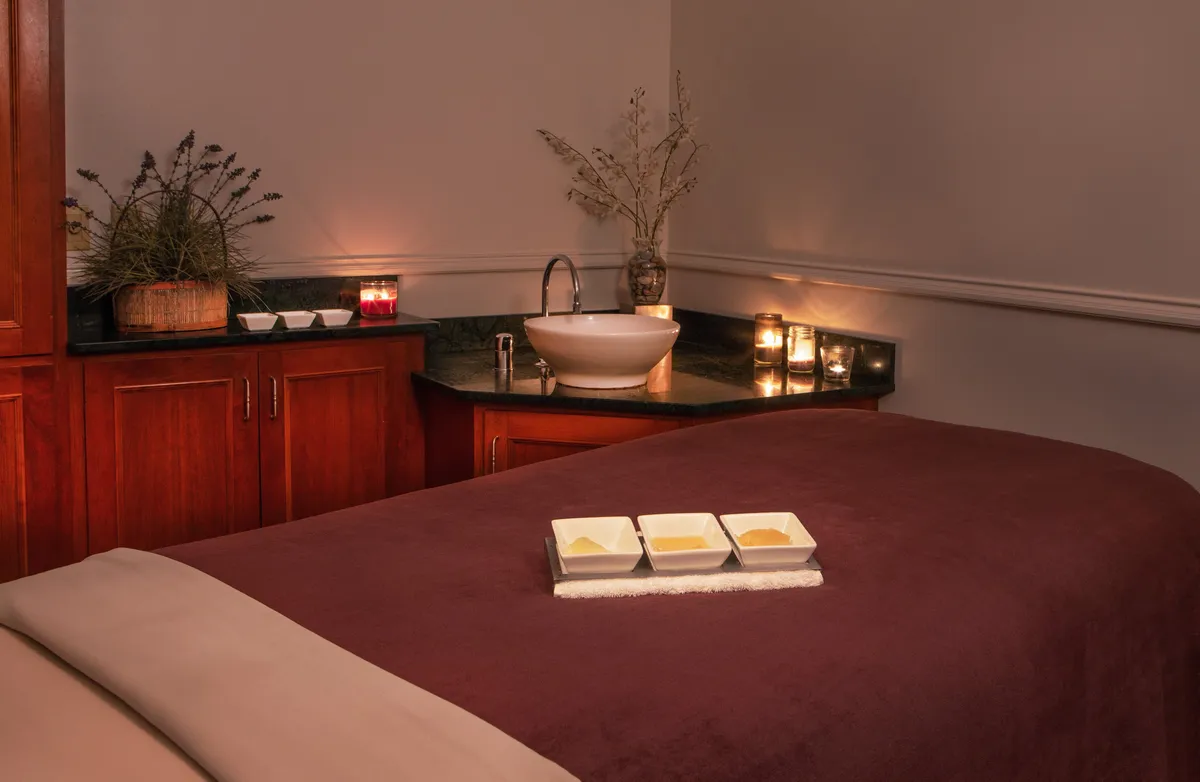 A calming spa treatment room with a massage table, soft lighting from candles, a decorative plant, and all the elements needed for a personalized wellness session.