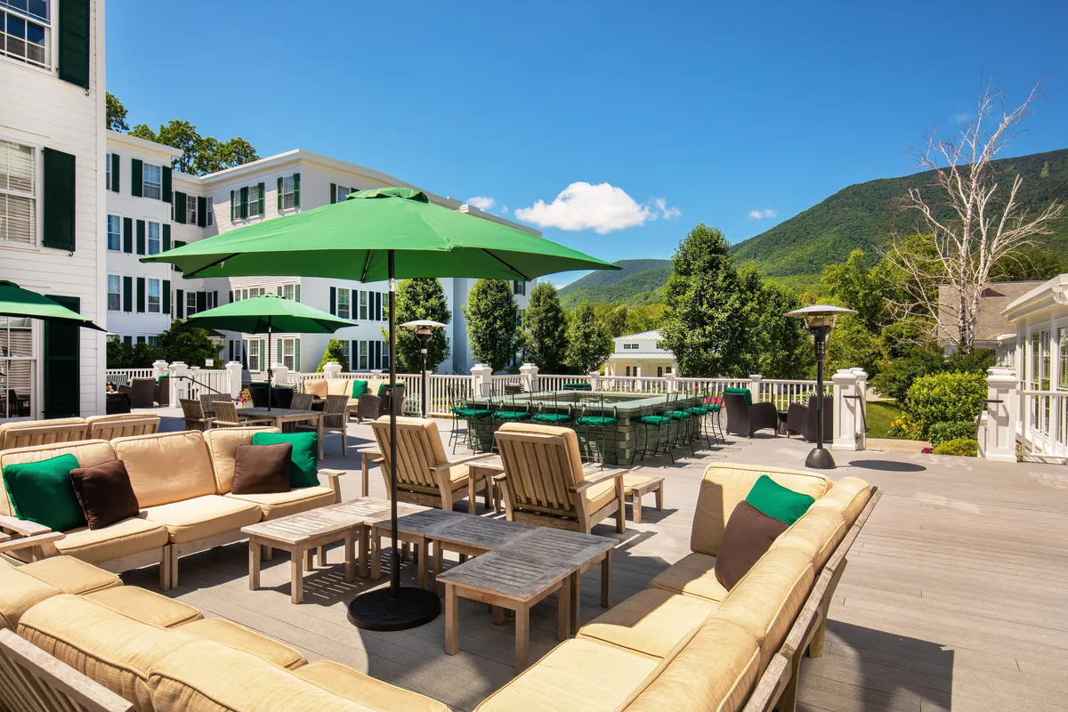 This exterior shot highlights an outdoor lounge and dining area set against mountain views, with green umbrellas and comfortable seating. The space is designed for socializing, enjoying fresh air, and casual gatherings with family or friends.
