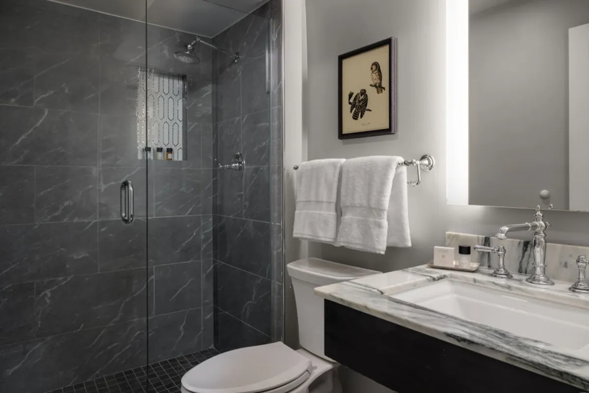 A sleek, modern bathroom with a glass shower enclosure, marble countertop, and framed artwork, evoking a peaceful, spa-like atmosphere. The space is well-lit and designed for relaxation and personal comfort.