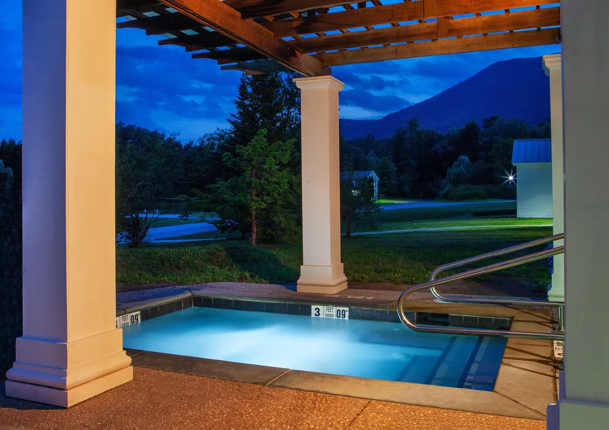 This exterior image showcases the inviting swimming pool area with a picturesque mountain view in the background. A stylish pergola structure offers a space for outdoor gatherings and relaxation, while the calm water and open sky evoke a sense of serenity and retreat.